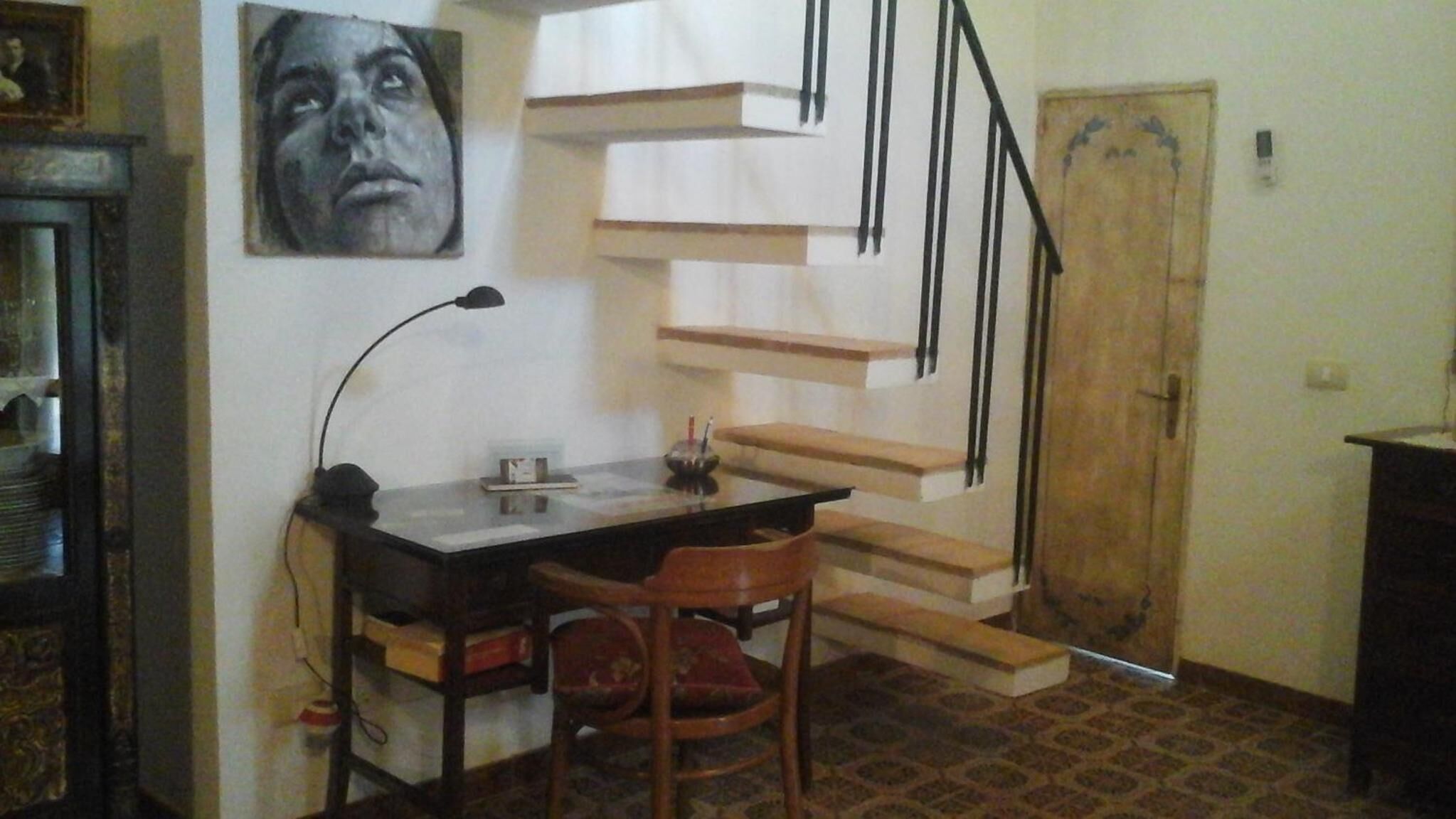 Ein Zimmer mit Schreibtisch, Stuhl und einer Treppe.