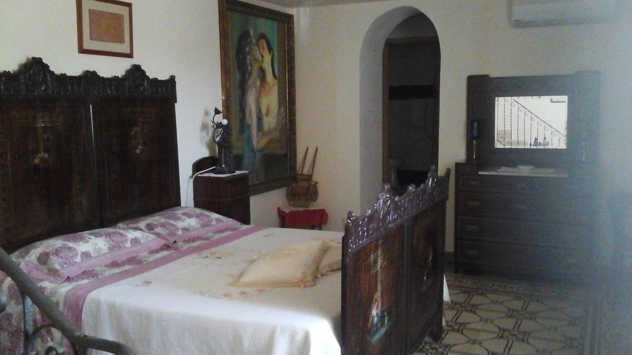 A bedroom with a bed, a dresser, a painting, and a mirror.