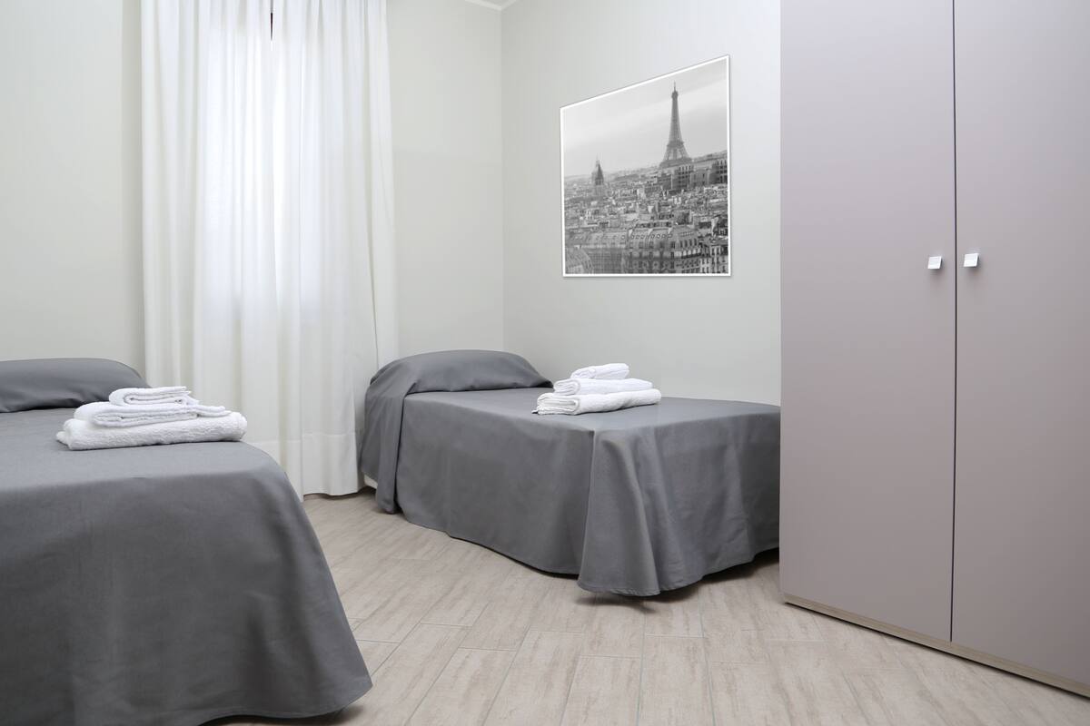 Habitación de hotel con dos camas, un armario y una fotografía de un paisaje urbano en la pared.