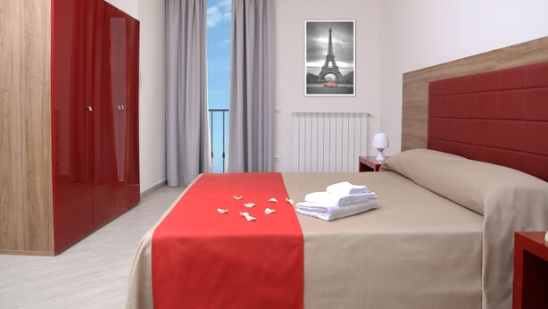 Habitación de hotel con cama, armario rojo, ventana con cortinas, radiador y un cartel del Torre Eiffel.