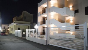 Un edificio moderno de varios pisos con entrada protegida, balcones iluminados y un coche estacionado afuera.