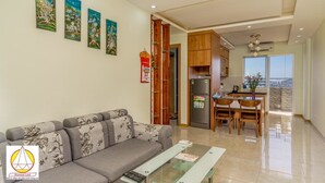 Una sala moderna con un sofá, una mesa de centro de vidrio y una zona de cocina con armarios de madera y un refrigerador.