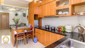 Una cocina moderna con armarios de madera, encimera negra y electrodomésticos de acero inoxidable. Hay una zona de comedor con una mesa y sillas, y un jarrón con flores sobre la mesa.