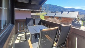 Een balkon met een tafel en stoelen, met uitzicht op een bergachtig landschap.