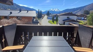 Uitzicht vanaf een balkon op een straat met huizen en bergen op de achtergrond.