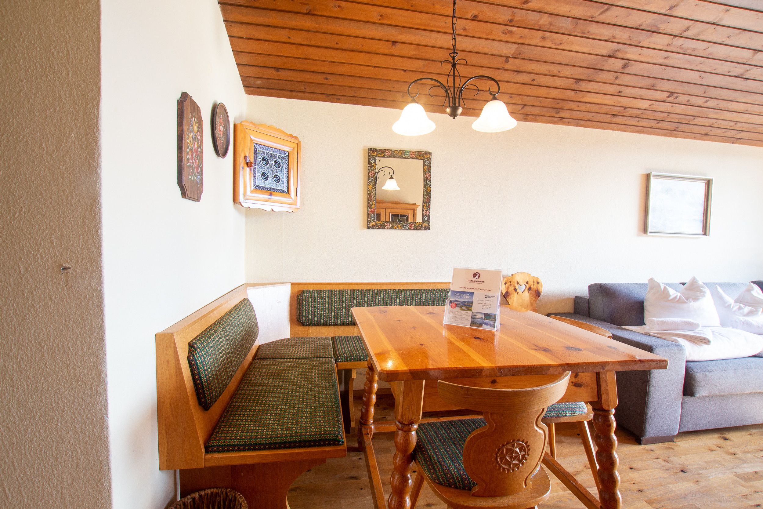Une table à manger en bois, accompagnée de bancs, d’un canapé et d’un lustre.