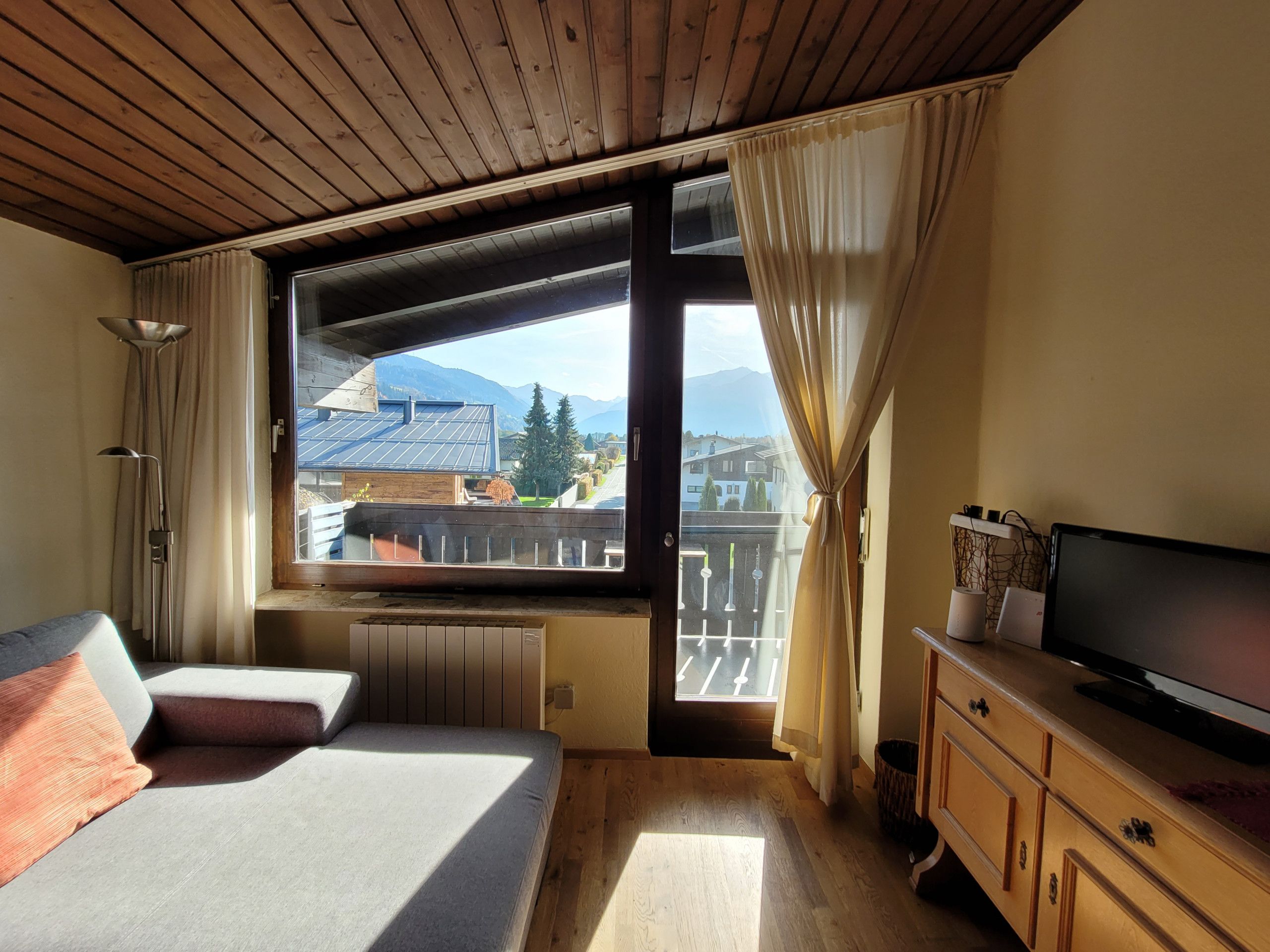 Ein Schlafzimmer mit Bett, Fernseher, Holzkommode und einem Fenster mit Vorhängen.