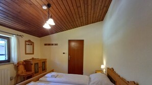 Een slaapkamer met twee bedden, houten hoofdborden, een houten dressoir, een spiegel en een deur.
