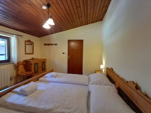 Un dormitori amb dos llits, amb capçaleres de fusta, un taulell de nit de fusta, un mirall i una porta.