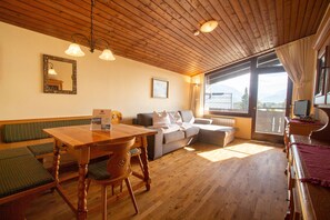 Une pièce chaleureuse avec un plafond en bois, une table à manger avec des chaises, un canapé et une grande fenêtre donnant sur l’extérieur.