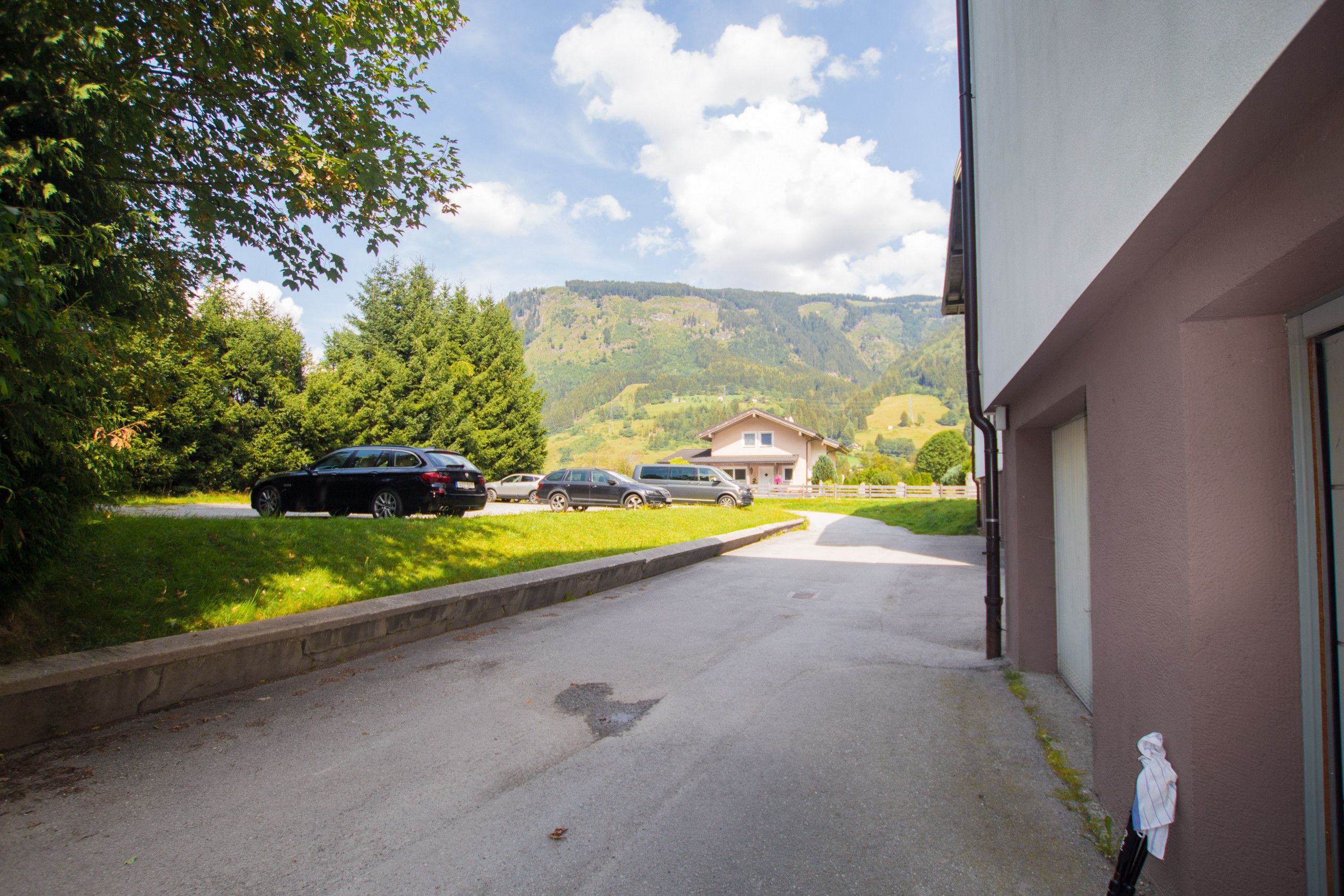 Une allée menant à un bâtiment d’où l’on peut admirer une montagne, avec des voitures garées devant.