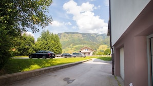 A driveway leading to a building with a view of a mountain and parked cars. - Apartment Schmid (Maishofen)