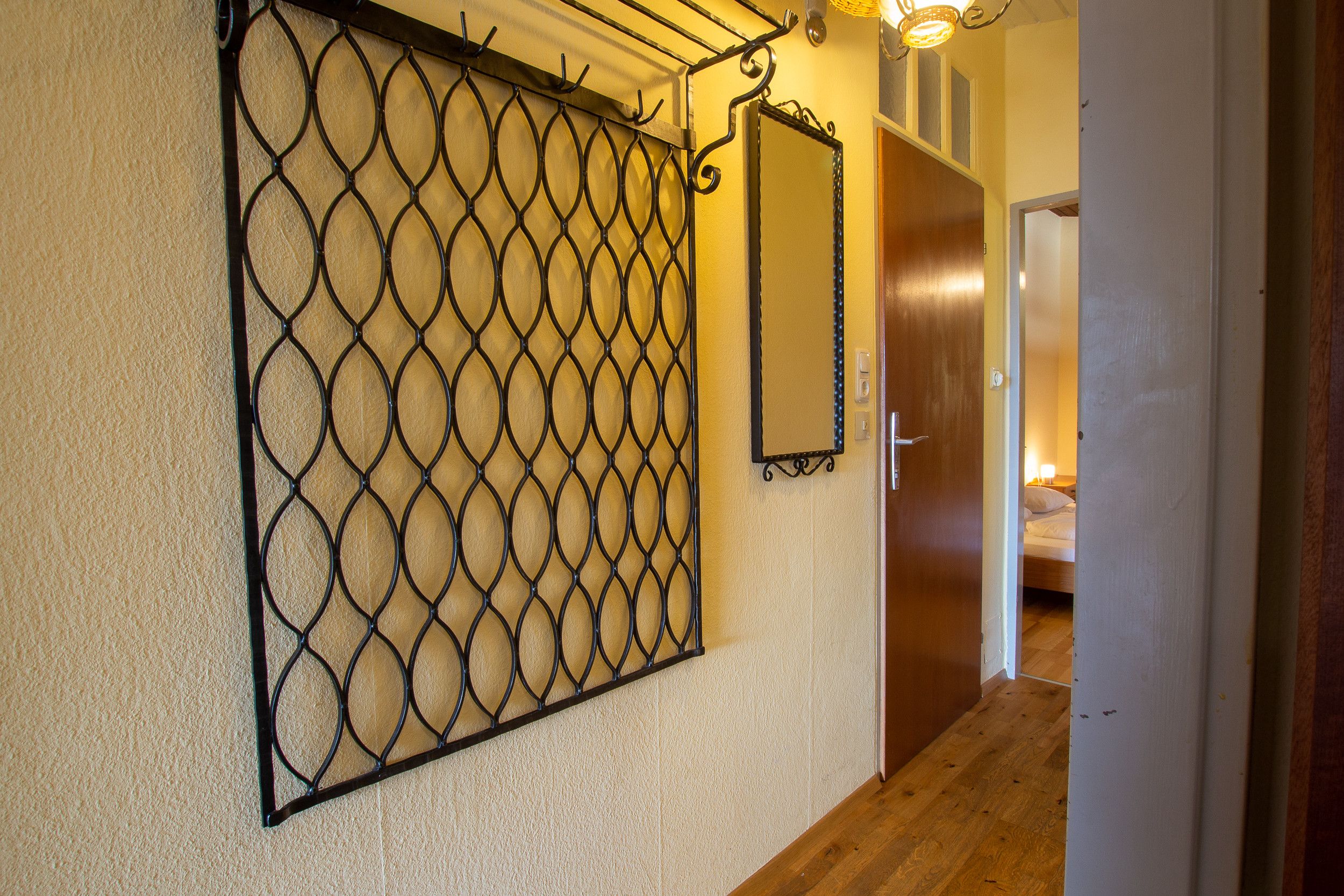 Un couloir avec une grille de sécurité en métal, une porte en bois et un lit dans la pièce adjacente.