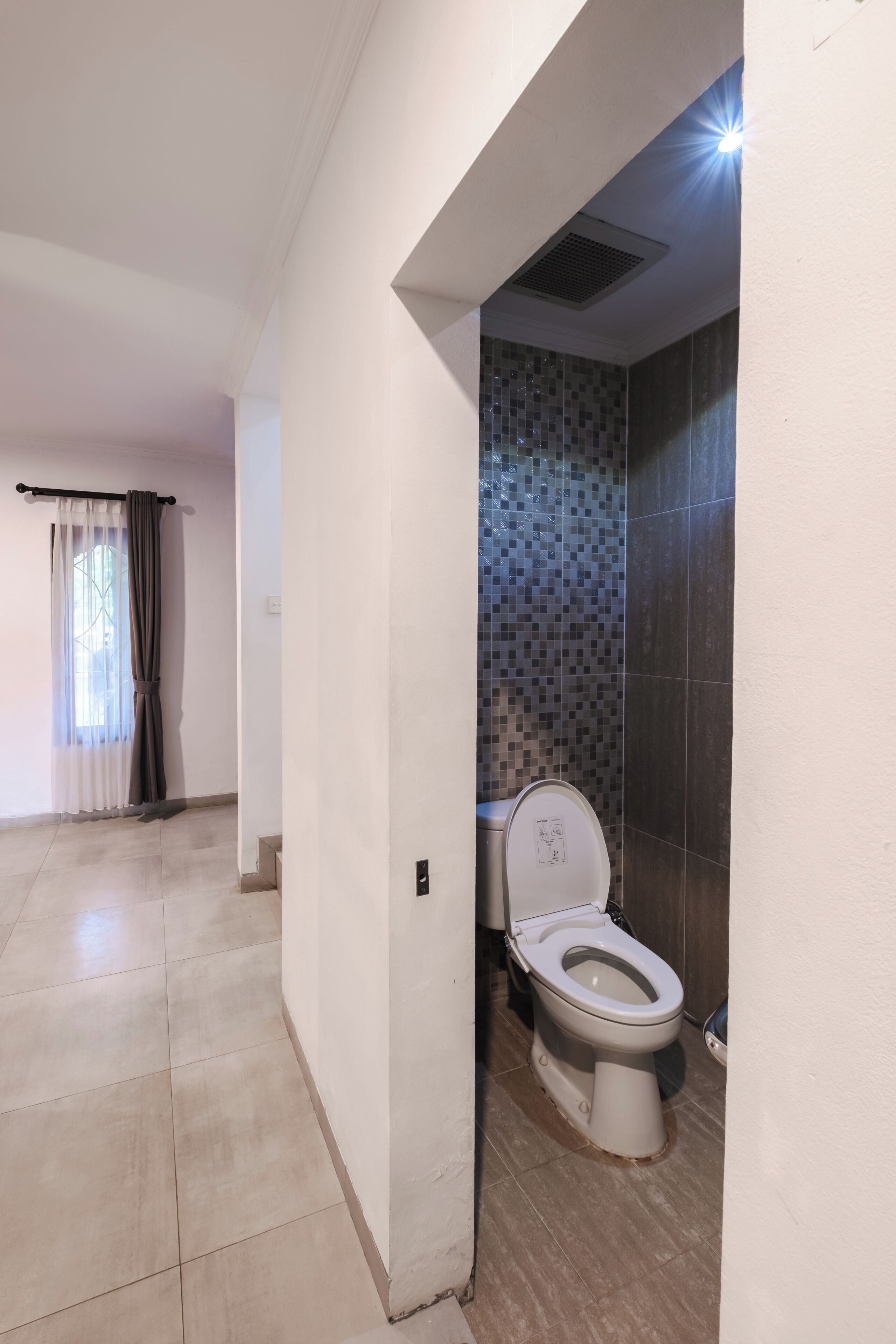 Ein Badezimmer mit Toilette, gefliesten Wänden und einem Fenster mit Vorhängen.