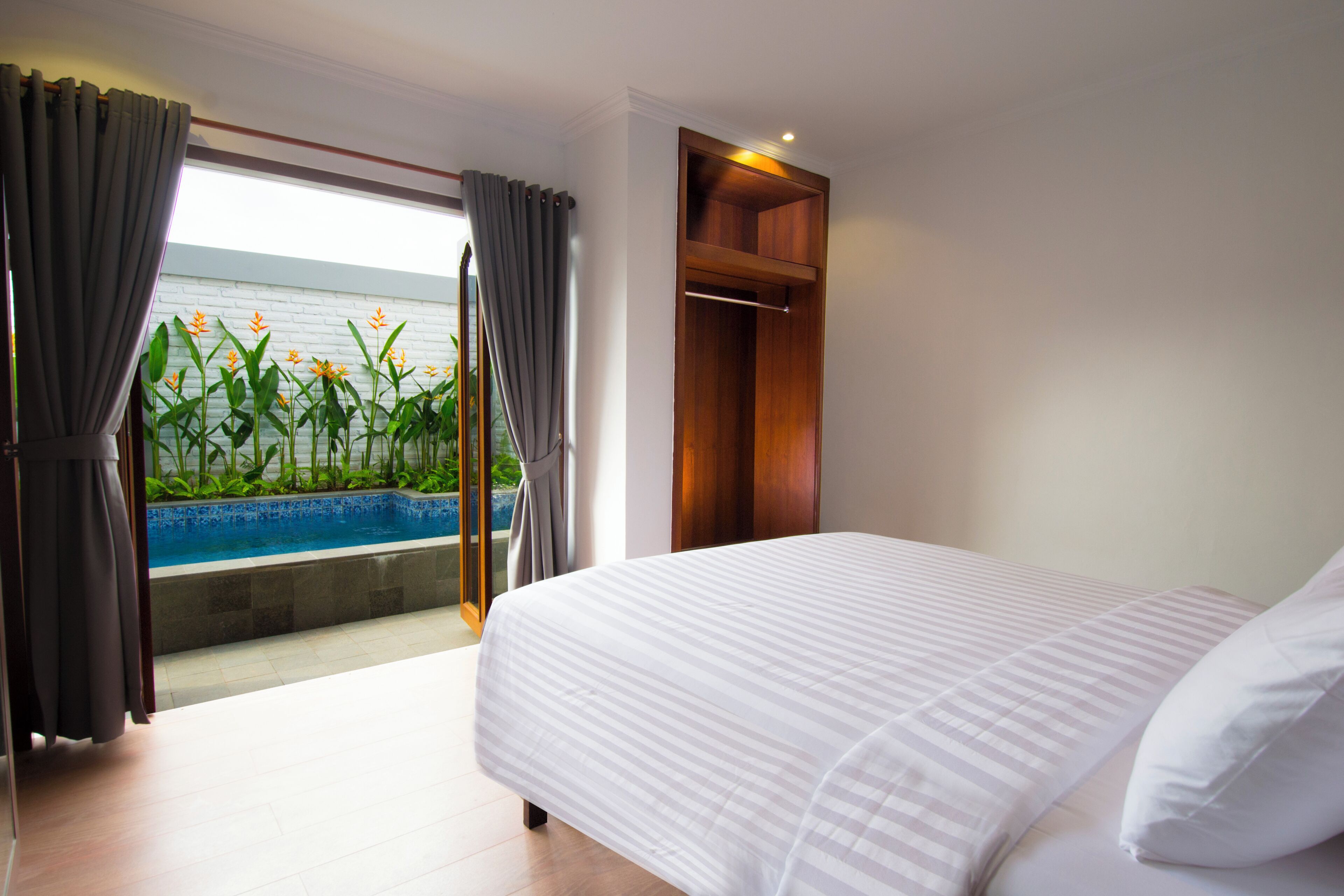 Un dormitorio con cama, armario de madera, vistas a una piscina y un balcón con cortinas.