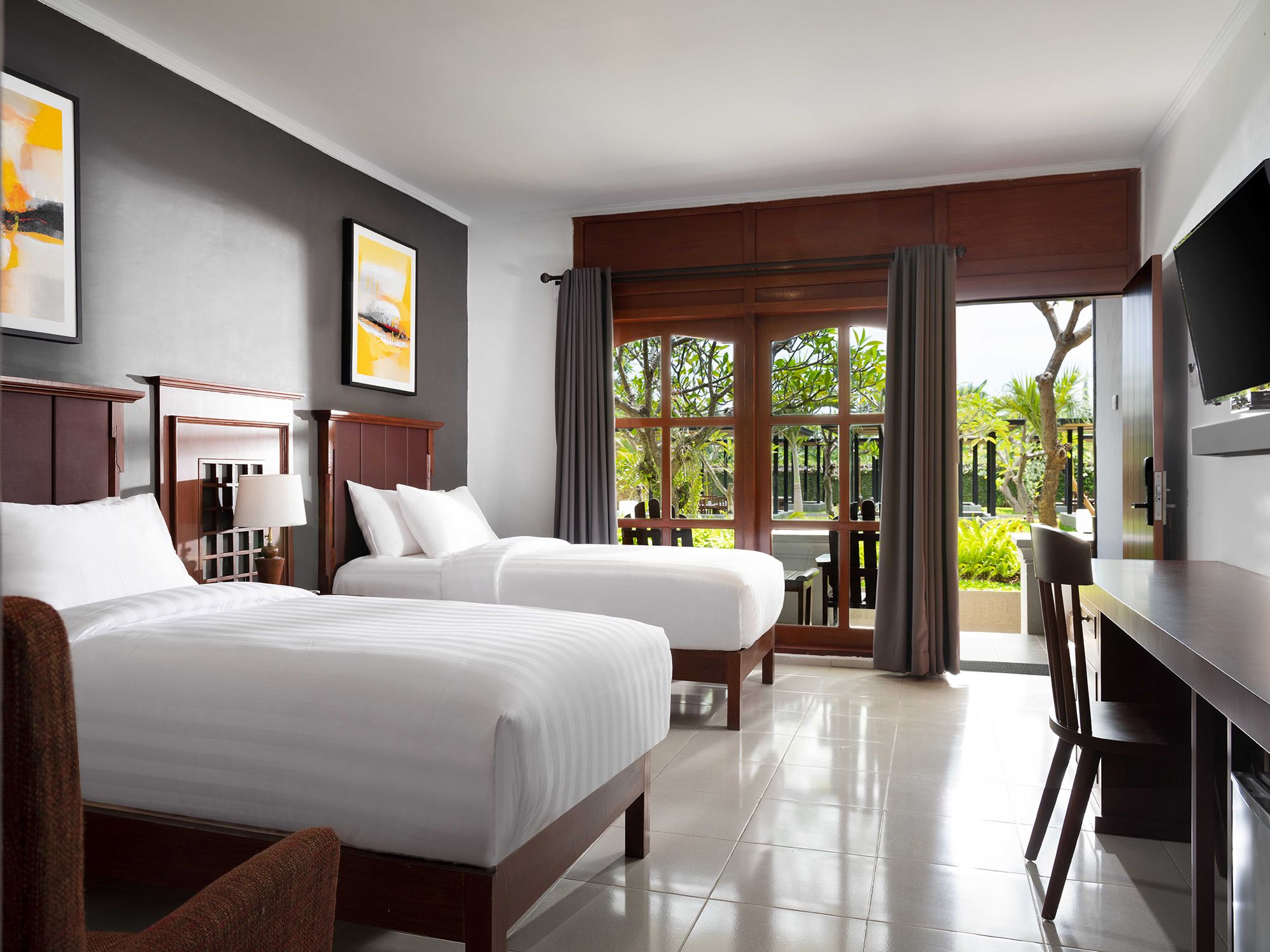 Habitación de hotel con dos camas, un escritorio, un televisor y vistas al exterior.