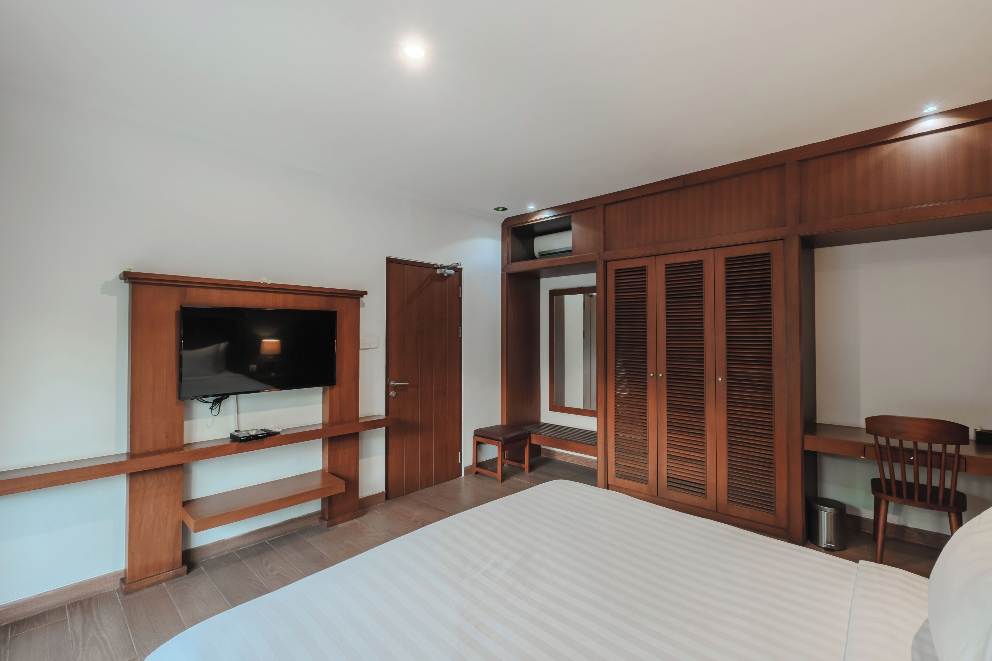 Un dormitorio con cama, televisor, escritorio, silla y armario.