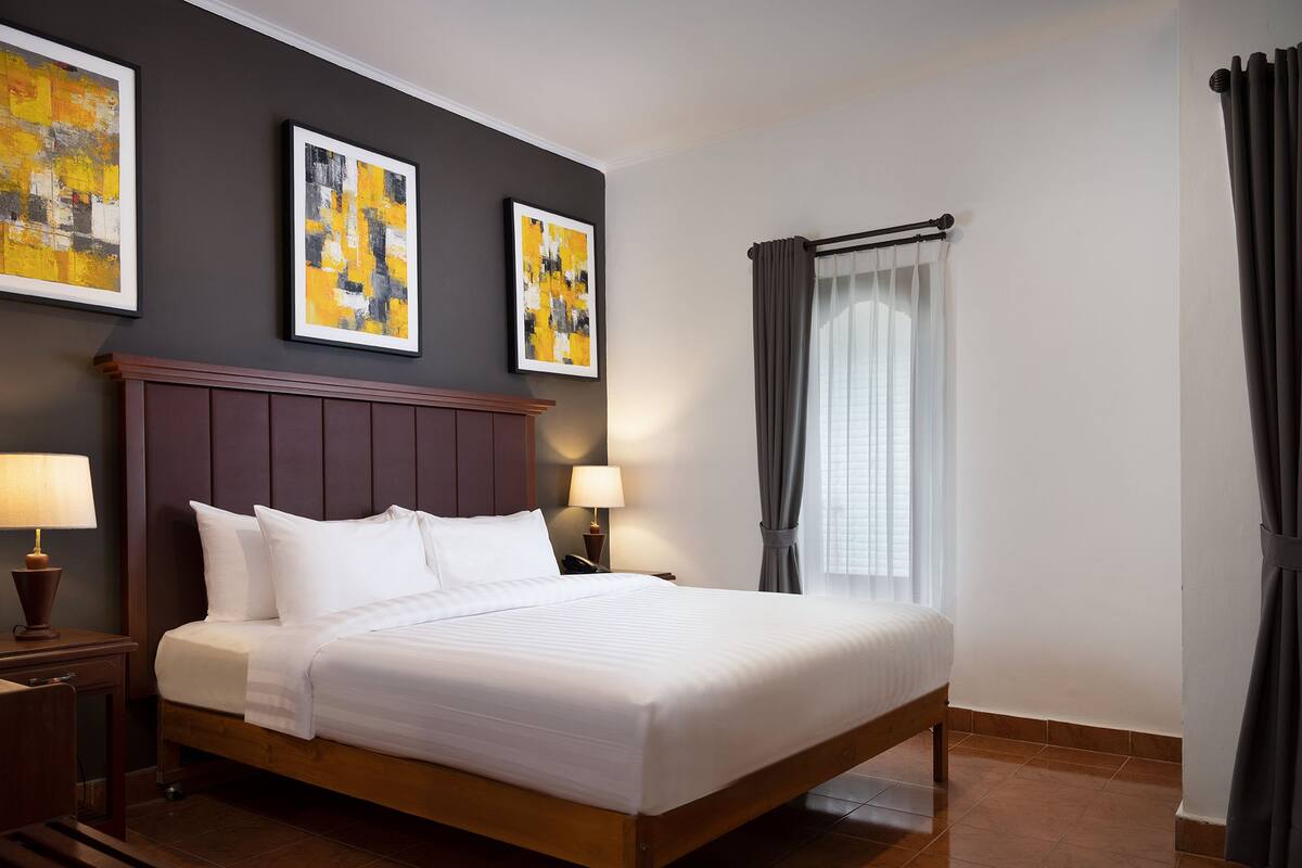 Un lit bien fait dans une chambre d’hôtel, avec une tête de lit en bois, deux tables de chevet avec des lampes et des œuvres d’art accrochées au mur.