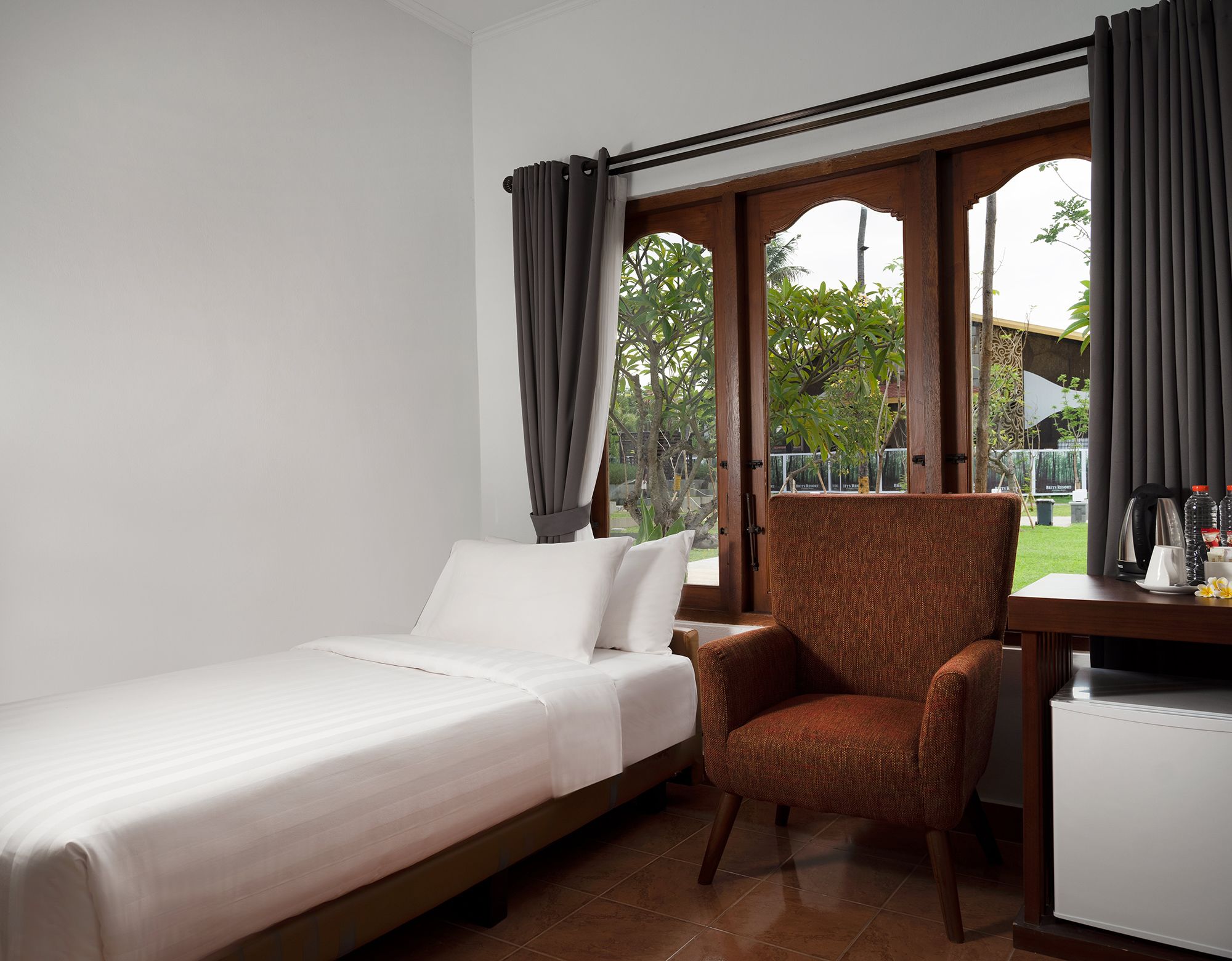 A room with a bed, a chair, a desk, and a window with curtains.