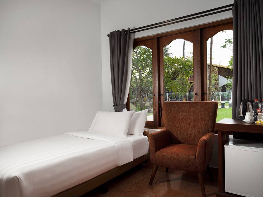 A room with a bed, a chair, a desk, and a window with curtains.