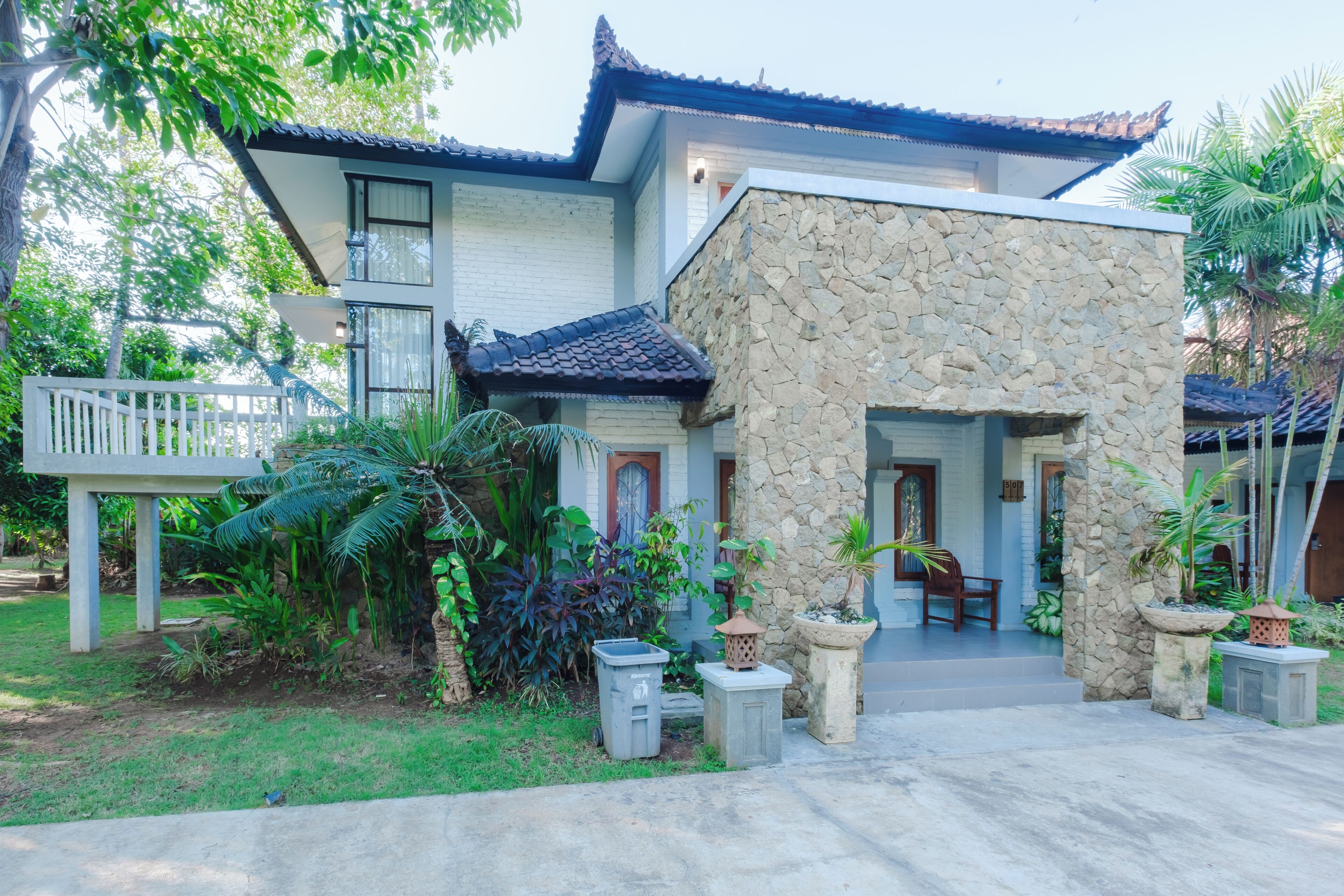 A two-story building with a stone facade, a tiled roof, and a porch with chairs.