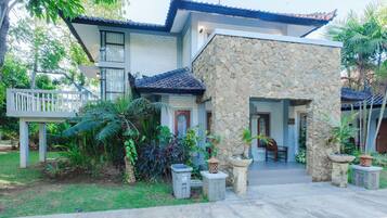 A two-story building with a stone facade, a tiled roof, and a porch with chairs.