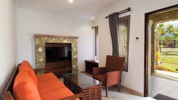 A living room with a stone fireplace, a flat-screen TV, orange sofas, and a glass coffee table.