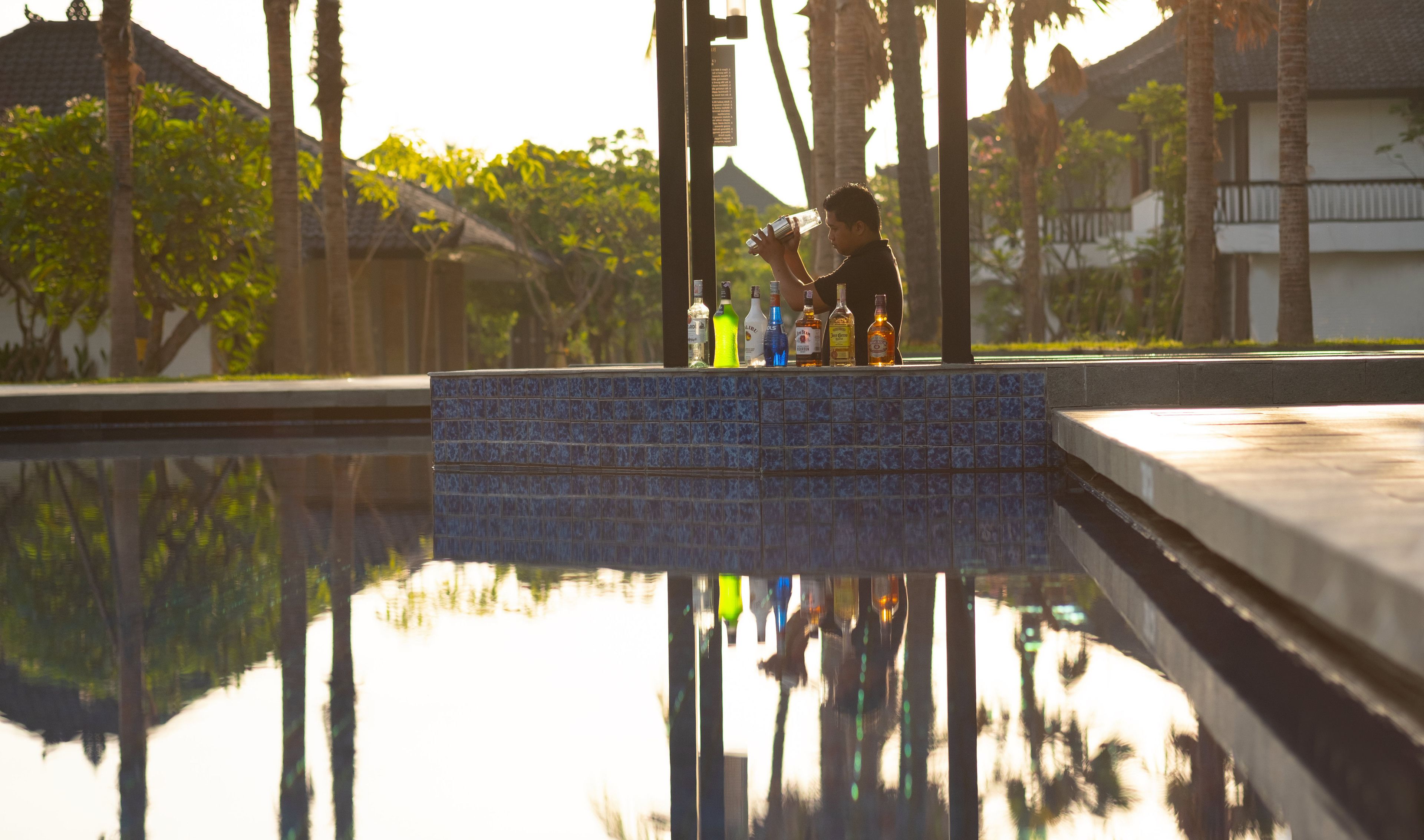 A pool with a tiled edge and a person holding a bottle.