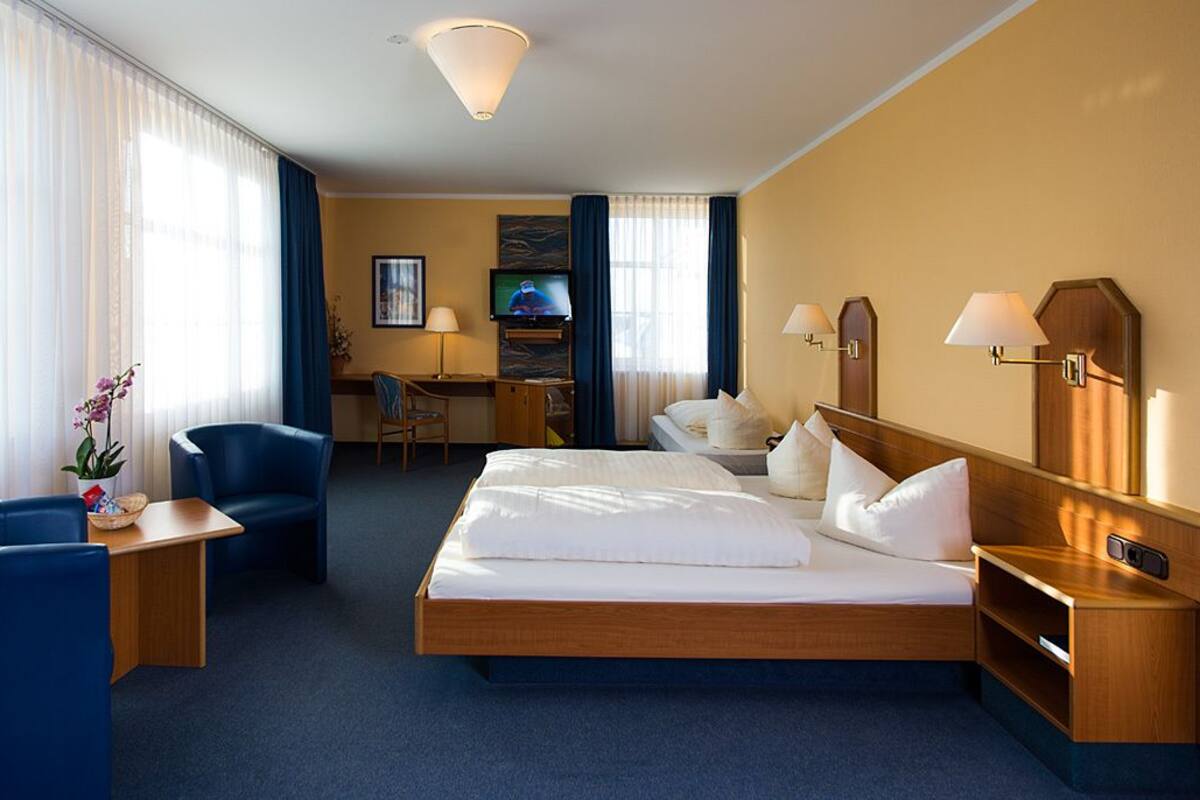 A hotel room with a bed, a desk, a chair, a TV, and a lamp.