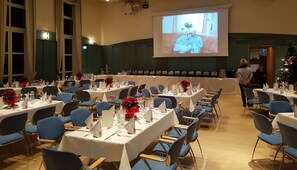 A conference room with rows of tables set for a meeting, a large screen at the front, and a Christmas tree in the background. - Hotel & Restaurant Residence (Bautzen)