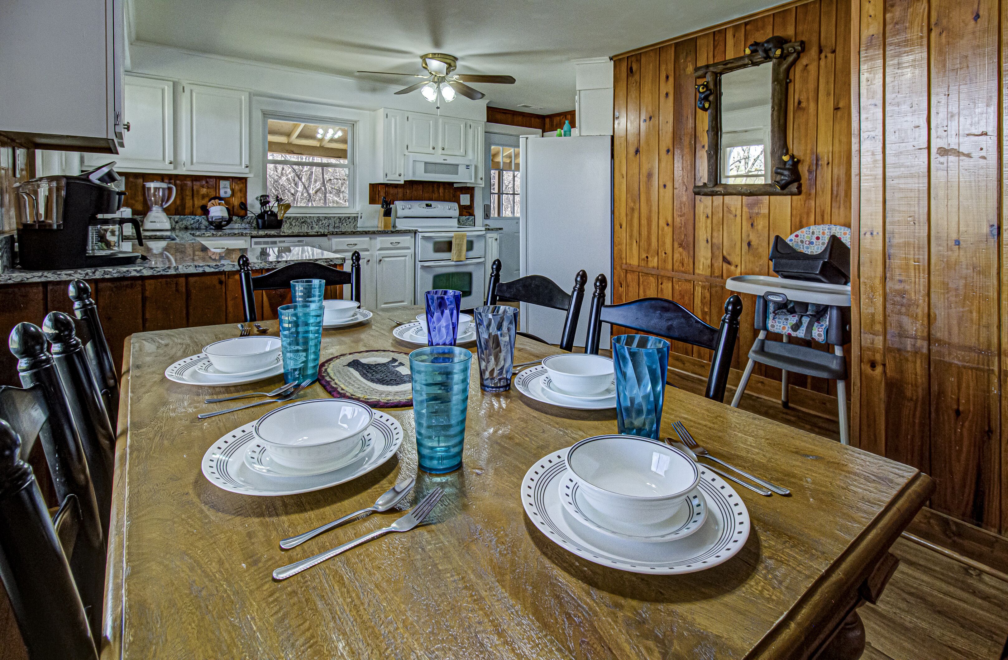 A dining area with a wooden table set for four, white plates, blue glass tumblers, and a ceiling fan.