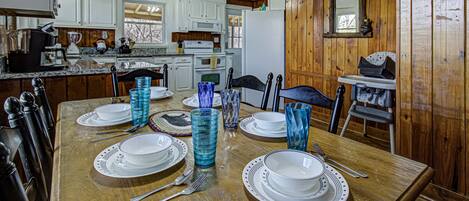 A dining area with a wooden table set for four, white plates, blue glass tumblers, and a ceiling fan.