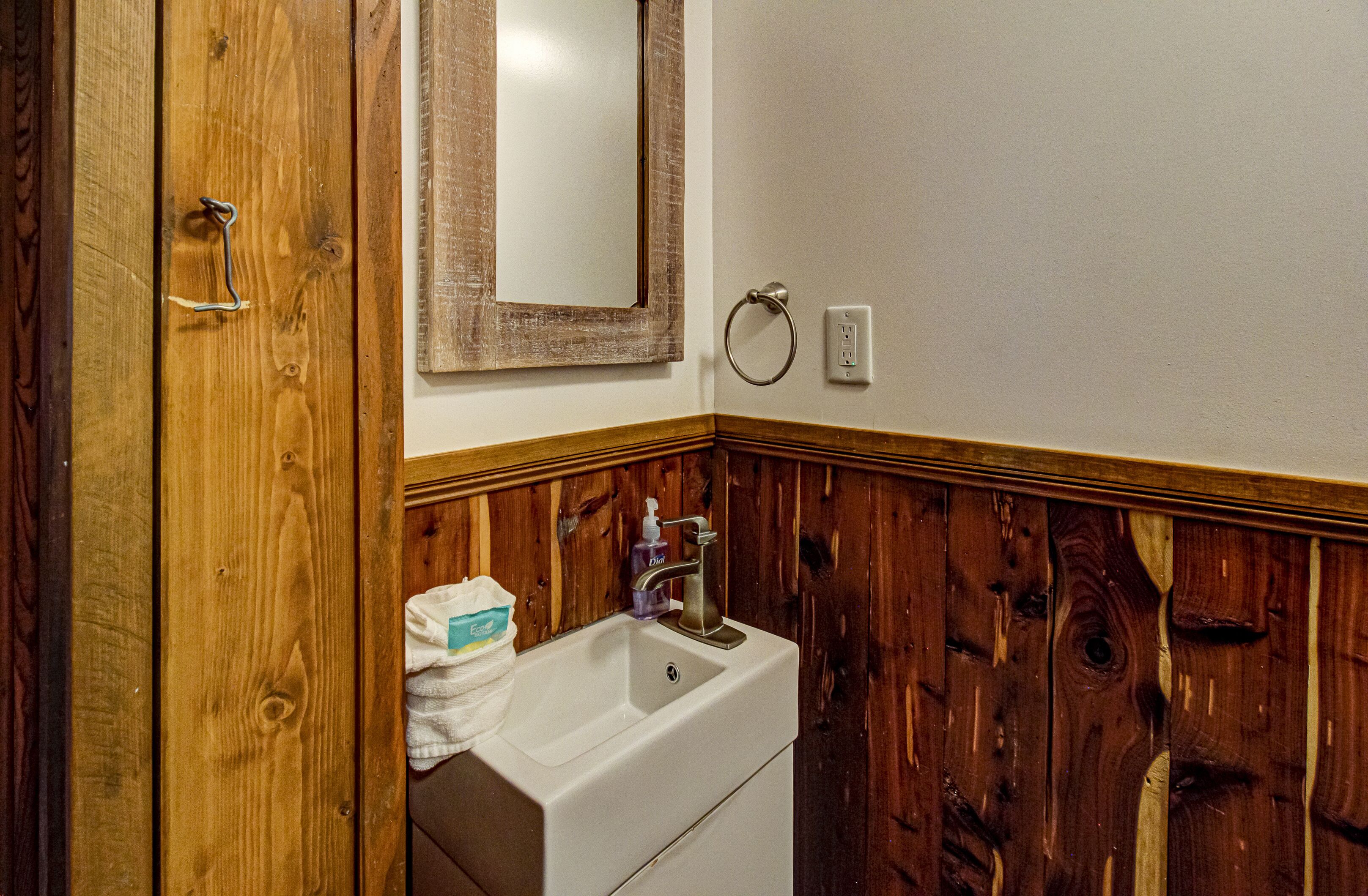 A bathroom with a wooden panel wall, a white sink, a mirror, and a towel dispenser.