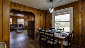 Une salle à manger aux murs lambrissés, avec une table dressée pour quatre personnes, un banc en bois à l’arrière-plan et une fenêtre donnant sur des arbres.