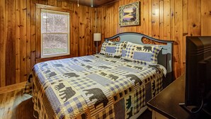 Une chambre à coucher aux murs lambrissés, avec un lit, une fenêtre, une lampe et un téléviseur.
