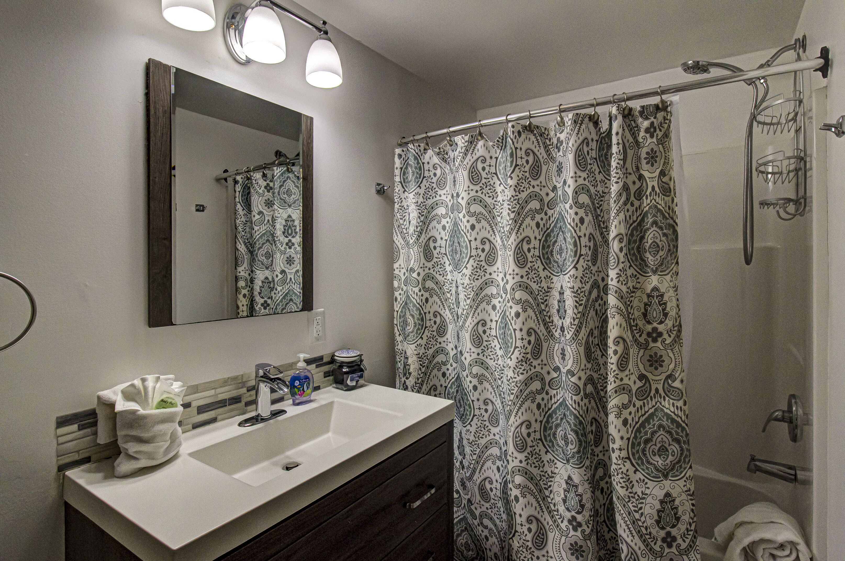 A bathroom with a large mirror, a sink, a shower, and a patterned shower curtain.