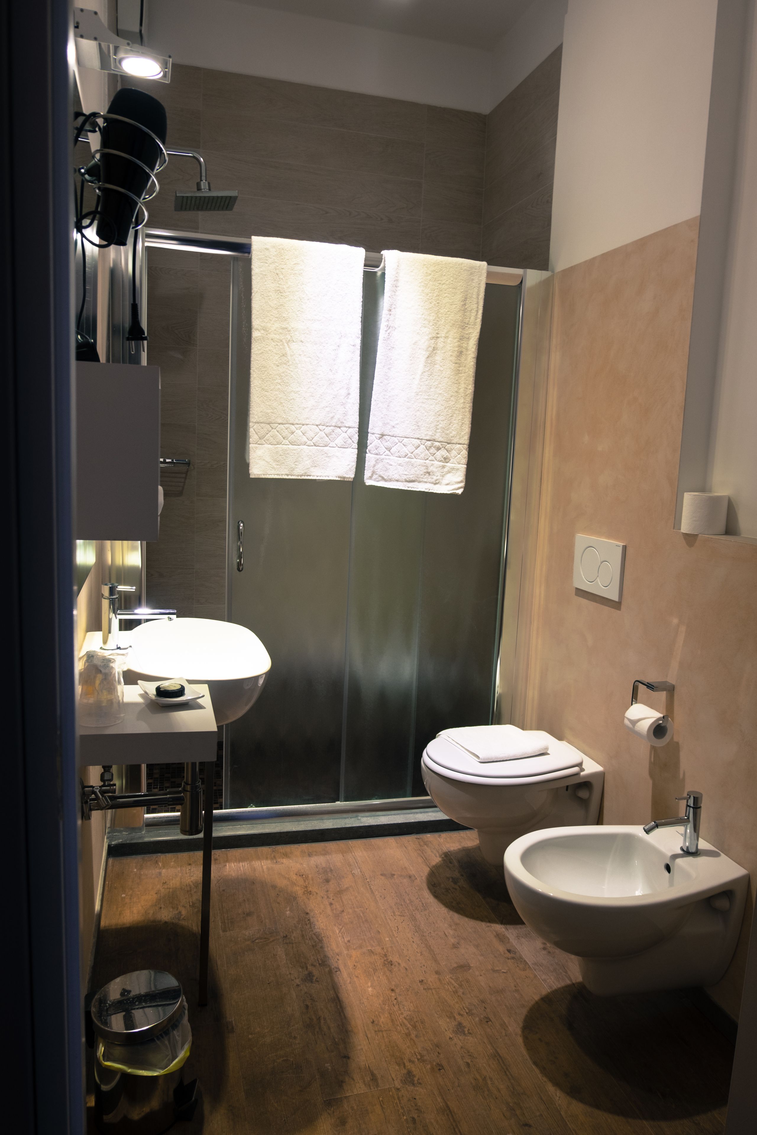 A modern bathroom with a glass shower enclosure, a sink, a bidet, and a toilet.