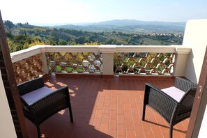 A balcony with two wicker chairs, terracotta tiles, and a view of green hills and distant mountains. - La Rocca Guest House & Spa (Montefalco)