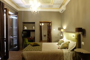 A hotel room with a bed, a desk with a chair, a television, and a chandelier. - La Rocca Guest House & Spa (Montefalco)