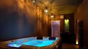 Quarto de spa com hidromassagem, iluminação suave e vista para um jardim através de uma janela.