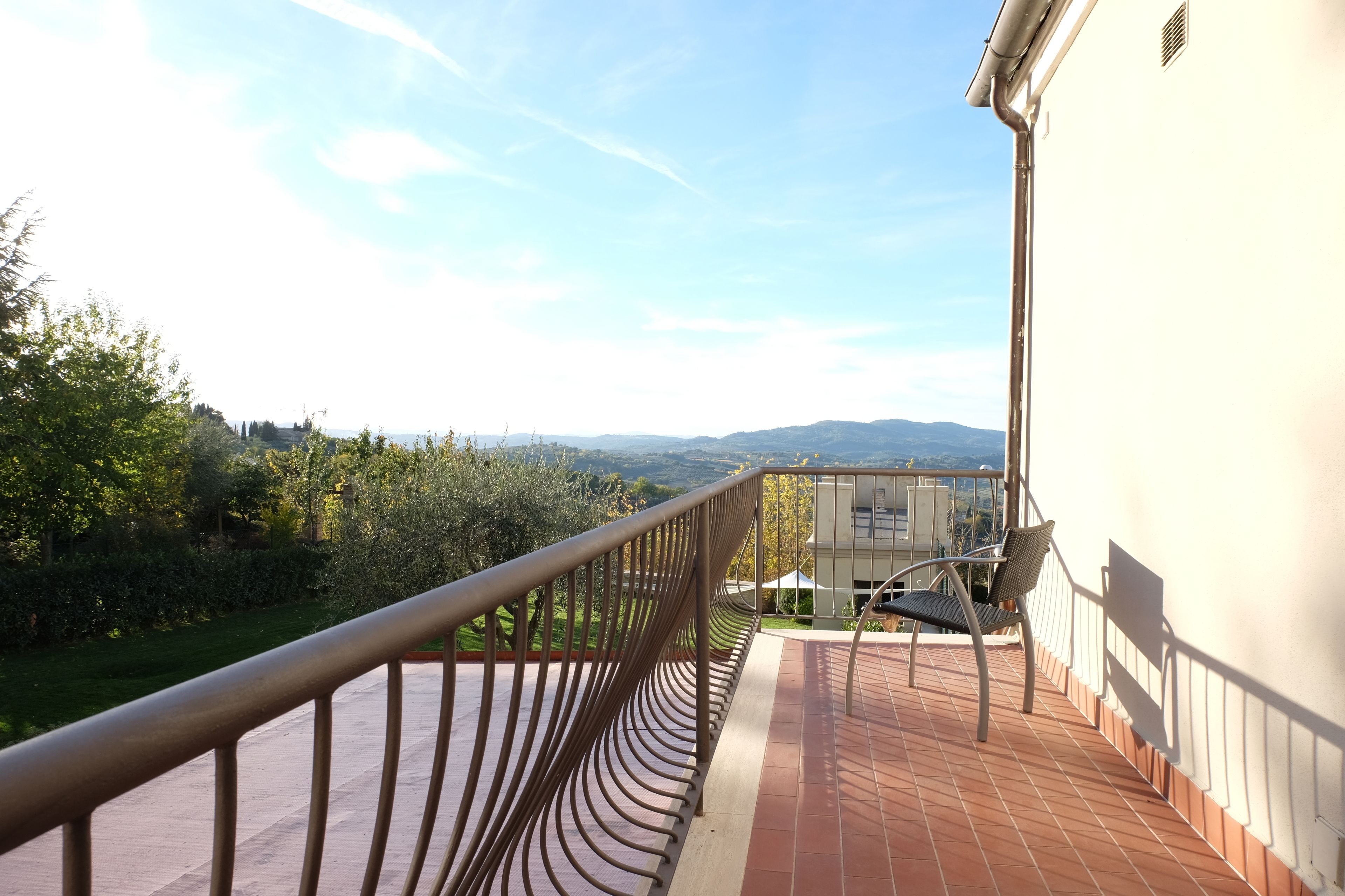 Un balcón con baranda de metal, una silla y vistas a un paisaje verde y colinas distantes.