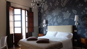 Quarto com cama grande, duas luminárias na parede, um lustre e uma janela com cortinas.