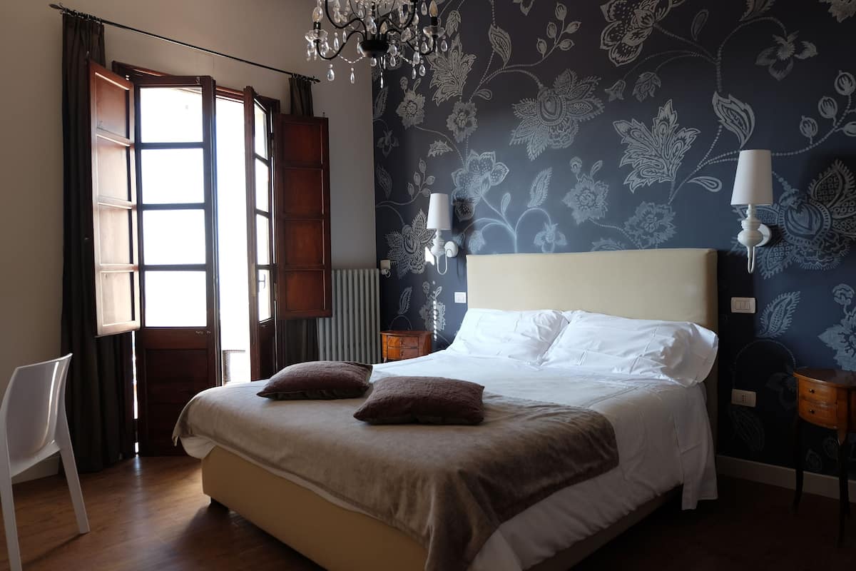 Un dormitorio con una cama grande, dos lámparas de pared, una araña y una ventana con cortinas.