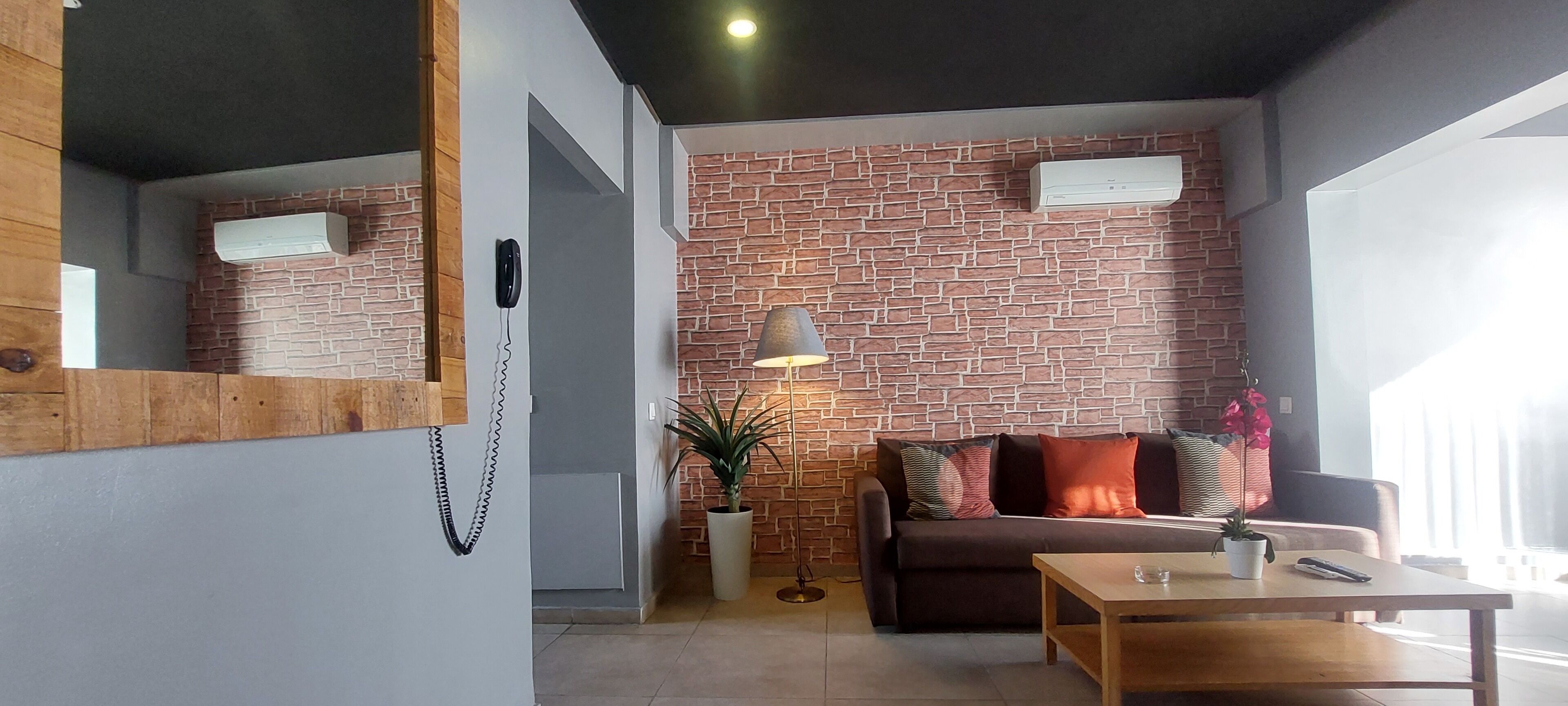 Un salon moderne avec un mur décoré d’un motif en briques, un canapé, une table basse et une lampe.