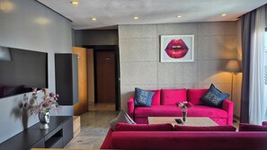 Un salon moderne avec un canapé rouge, un téléviseur à écran plat et un tableau représentant des lèvres accroché au mur.