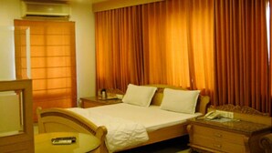 A hotel room with a bed, a bedside table, a chair, a desk, and a window with curtains. - Sana Heritage Inn Hyd (Hyderabad)