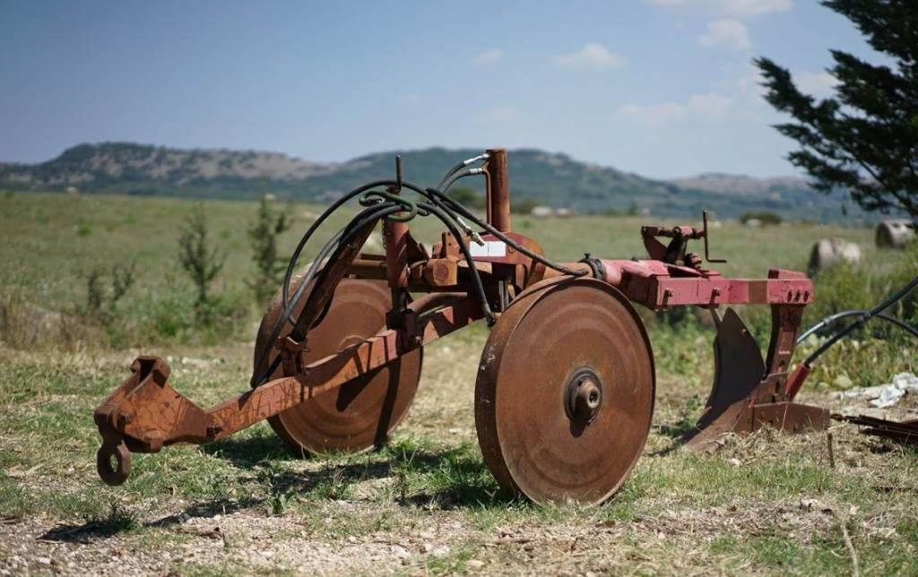 A vintage tractor in a field with mountains in the background.