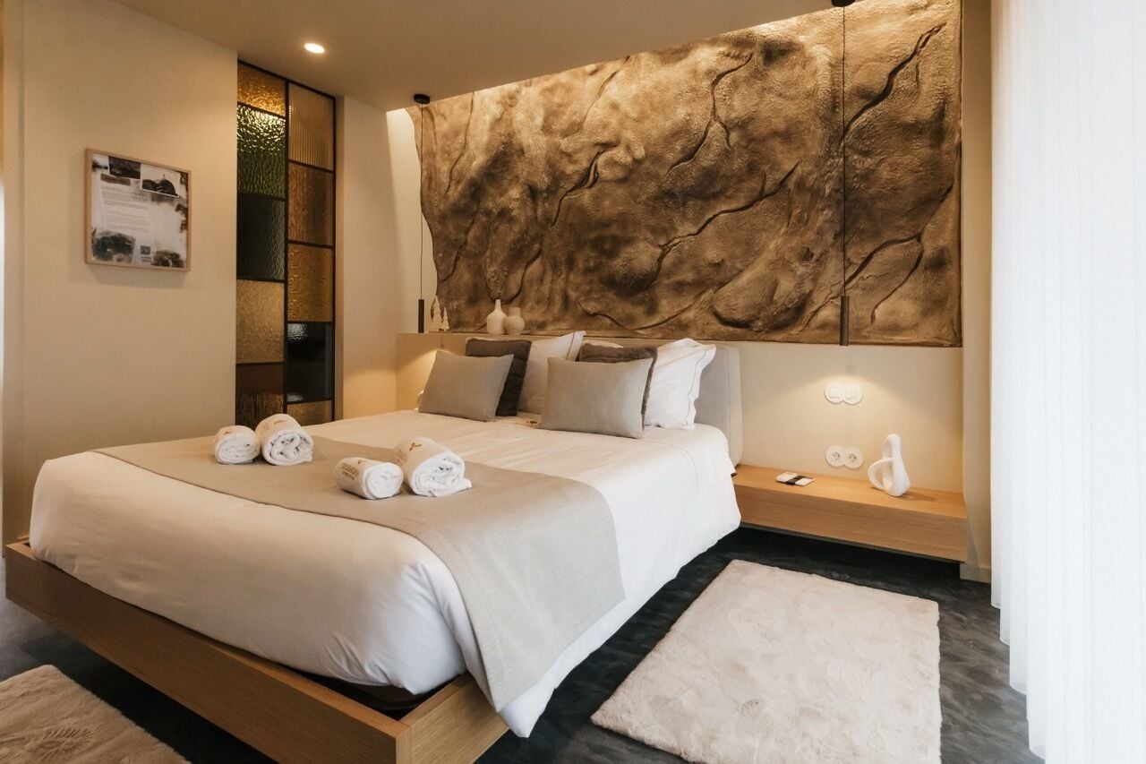 Habitació d'hotel moderna amb un llit gran, una tauleta de nit de fusta, una làmpada penjada a la paret i una taula petita amb un ram.