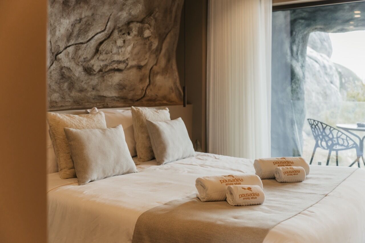 A hotel room with a large bed, a stone wall, and a view of the outdoors.