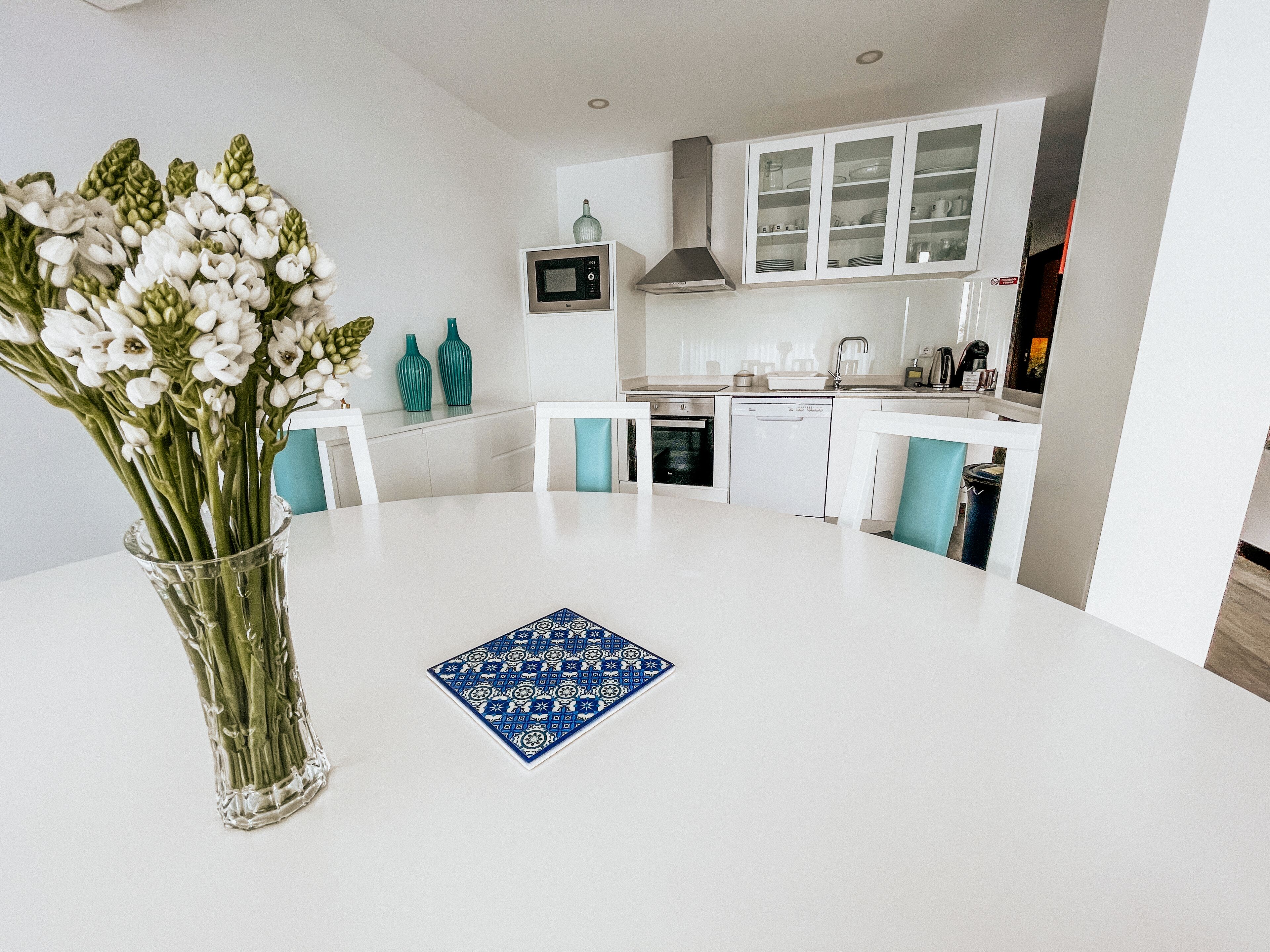A modern kitchen with white cabinets, a microwave, and a dishwasher. There is a vase with flowers on the table.